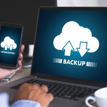 online backup cloud service spideroak one man backing up content on laptop holding smartphone white cup of coffee near laptop 